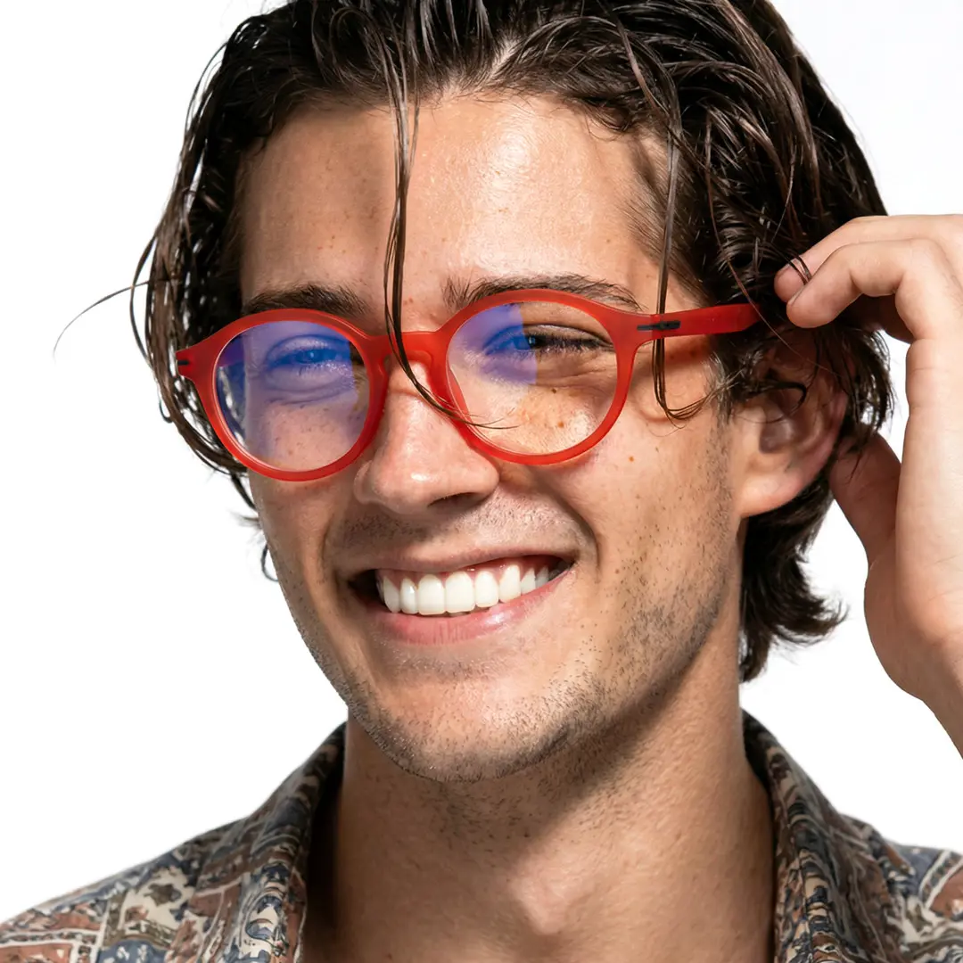 Three-quarter view of male wearing red round eyeglasses, holding glasses, smiling, RR0052412