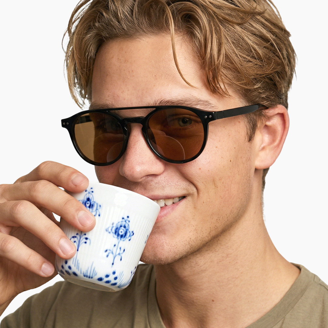 Slightly angled view of male wearing black round magnetic clip-on eyeglasses set with brown clip-on lenses, hand holding a cup, smiling, RR0132601