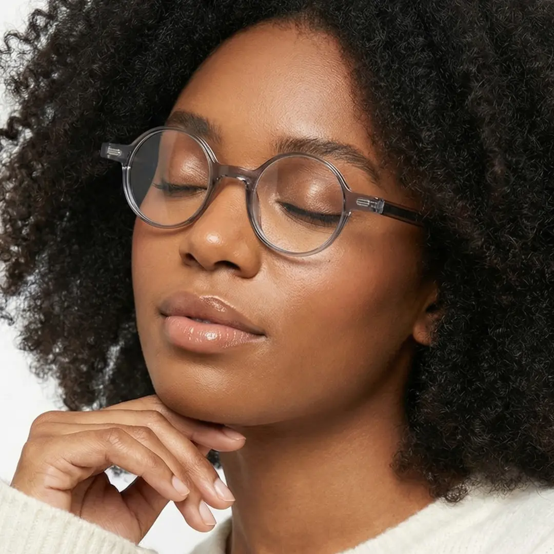 Profile view of female wearing vintage grey round eyeglasses, resting chin on hand, RR0162209