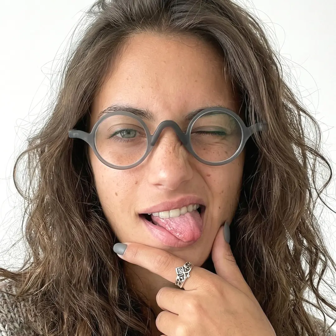 Front view of female wearing vintage grey round eyeglasses, sticking out tongue, neutral expression, RR0282410