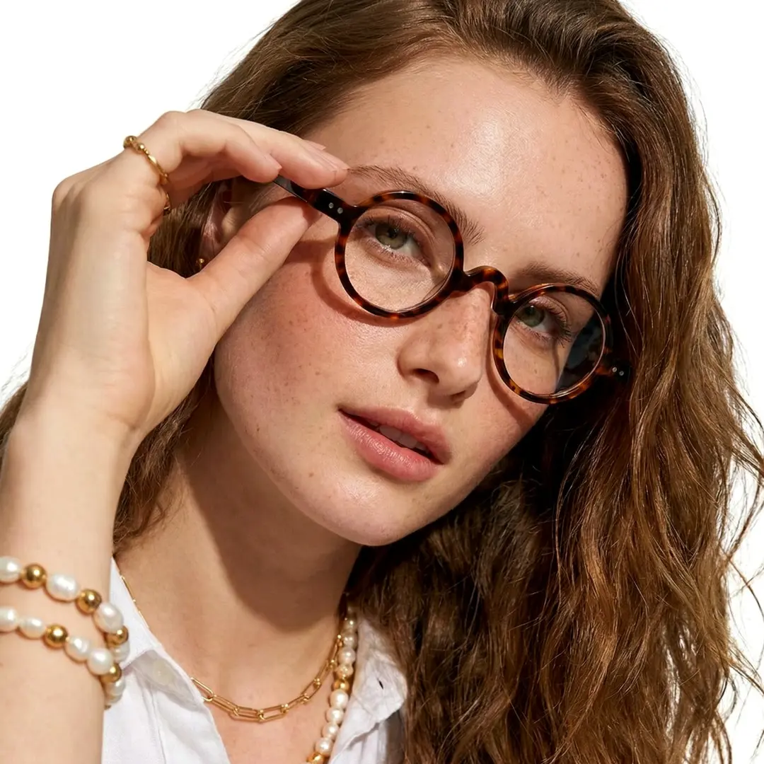 Front view of female wearing vintage tortoise round eyeglasses, touching frame, neutral expression, RR0322601