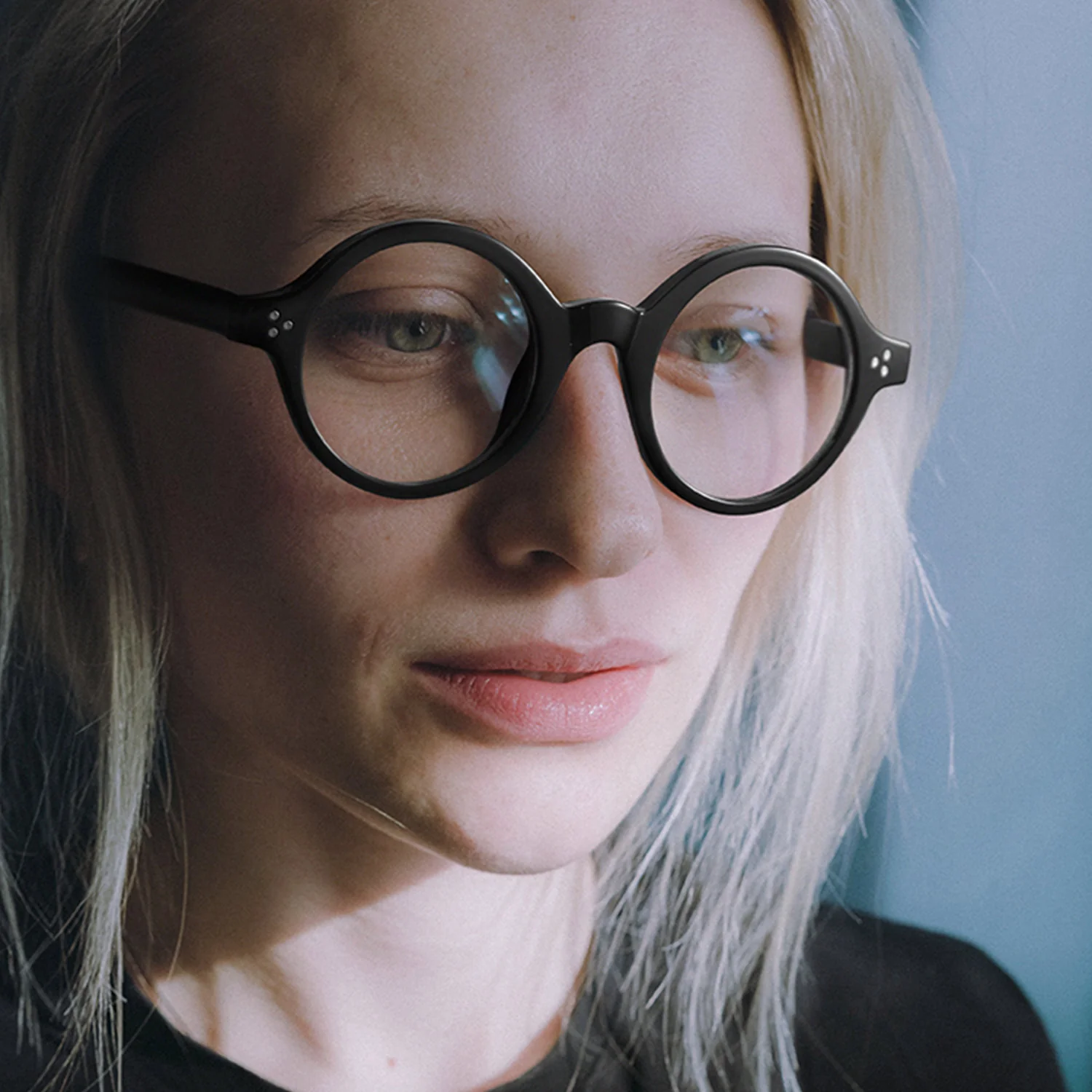 Looking away view of female wearing black round eyeglasses, neutral expression, RR0352302