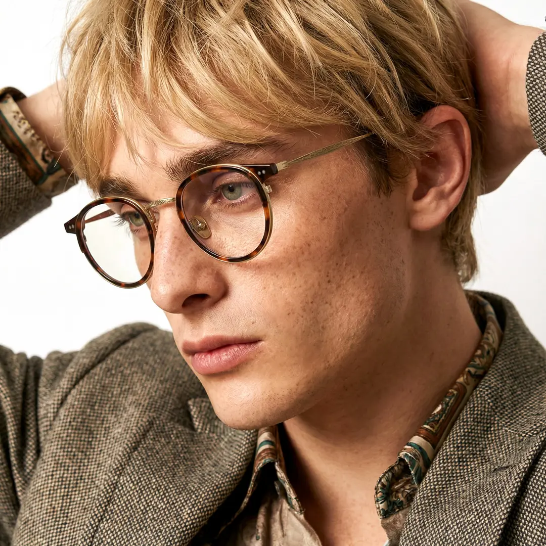 Looking away view of male wearing vintage tortoise round eyeglasses, hand in hair, neutral expression, RT0022209