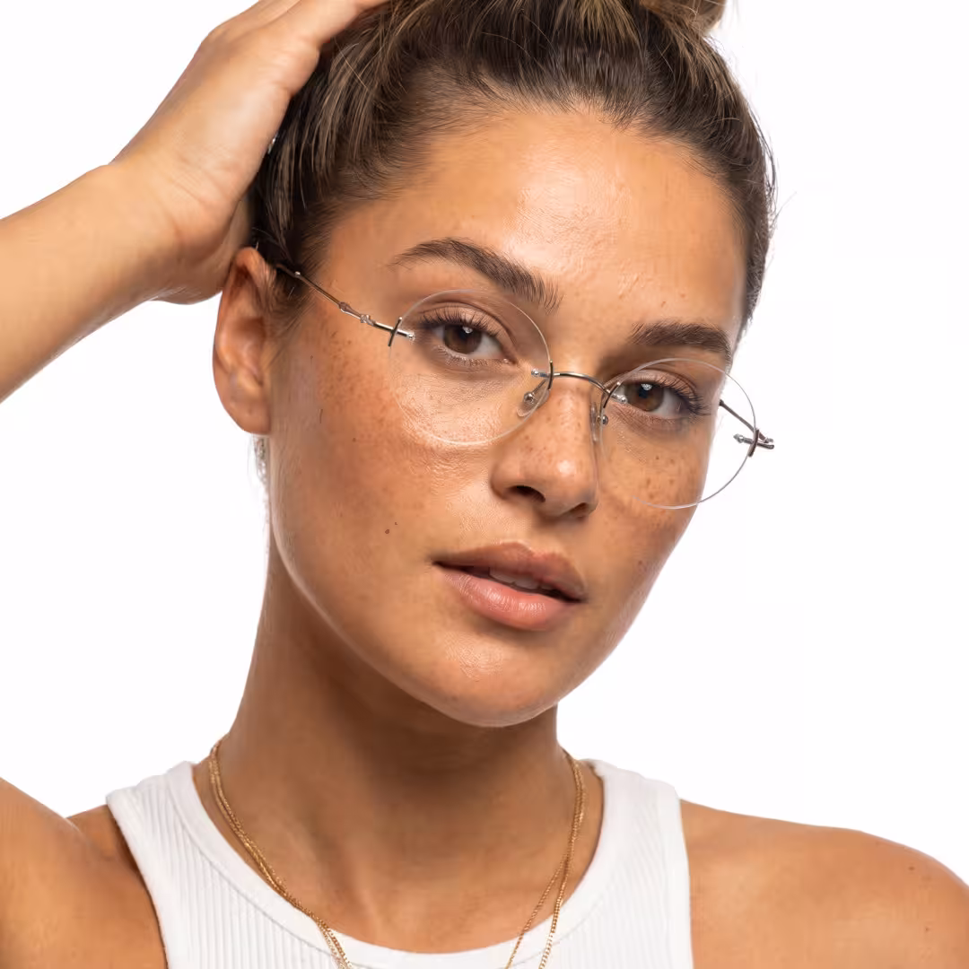 Female wearing steampunk silver round titanium eyeglasses, neutral expression while hand in hair. SPU: RT0262604