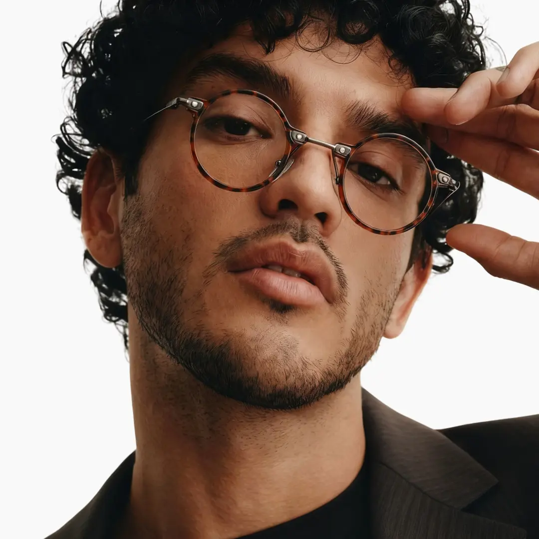Tilted head view of male wearing steampunk tortoise round eyeglasses, hand resting on forehead, neutral expression, RT0302405