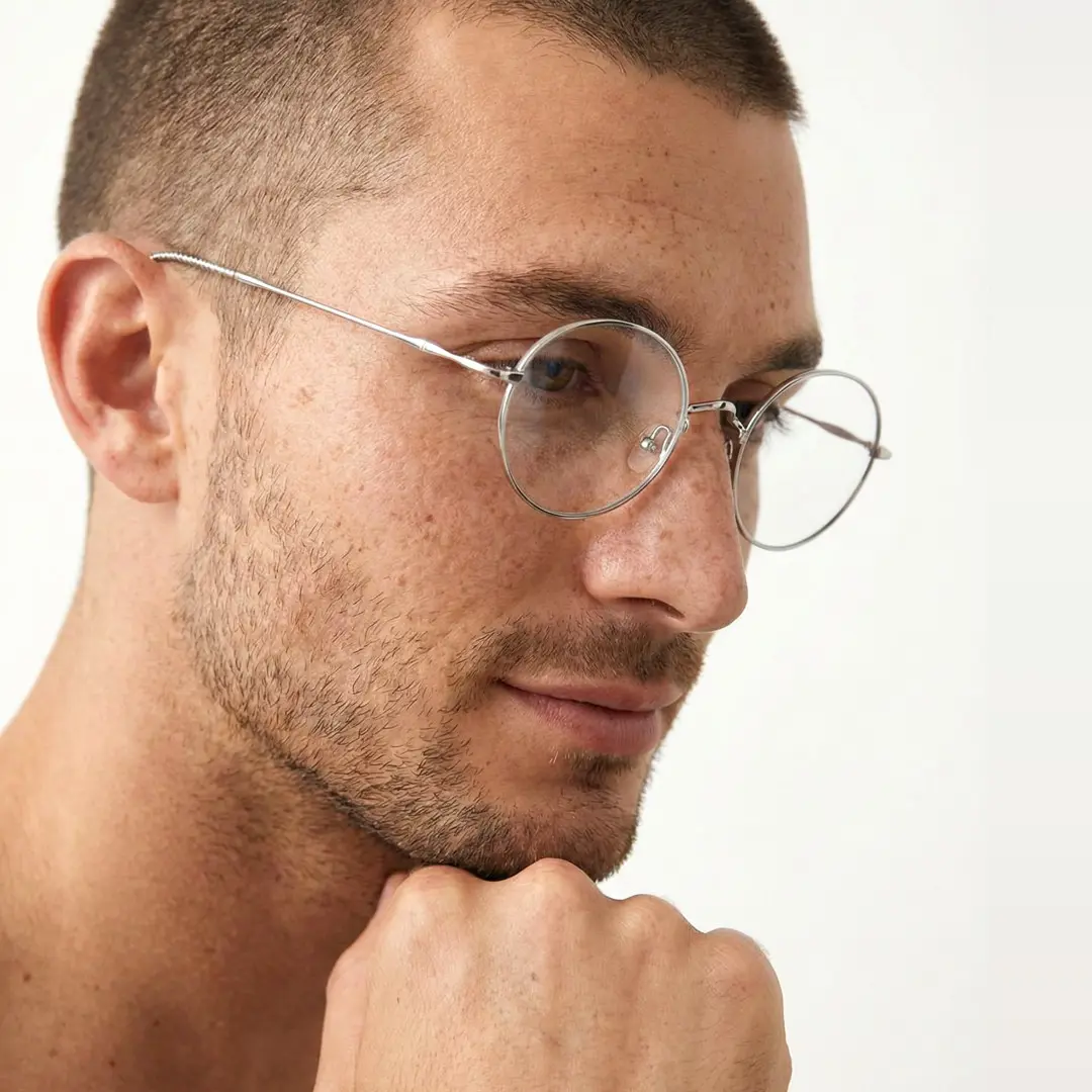 Front view of male wearing vintage silver round eyeglasses, resting chin on hand, soft smile, RT0942508