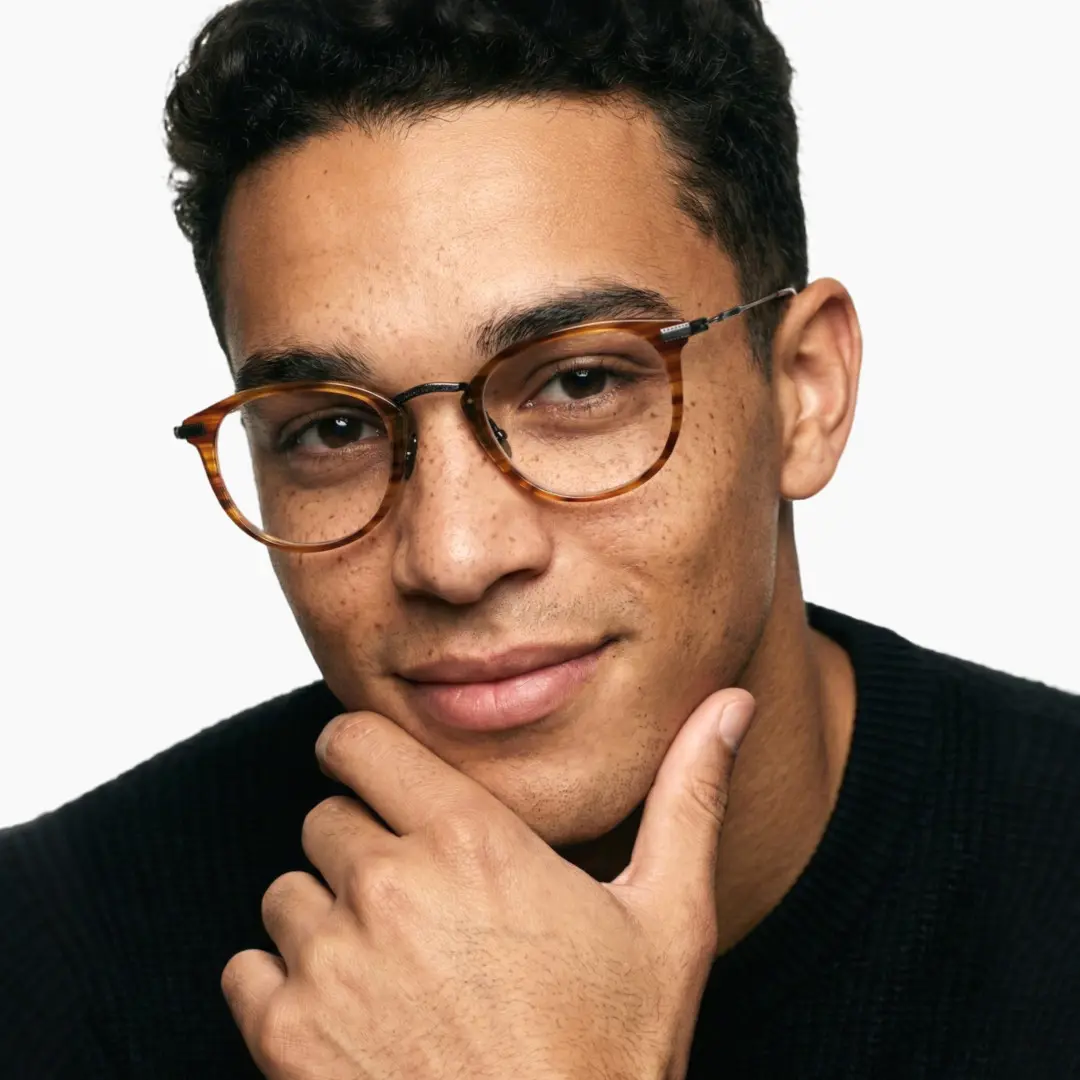 Three-quarter view of male wearing tortoise round eyeglasses, holding glasses, natural smile, RX0062207