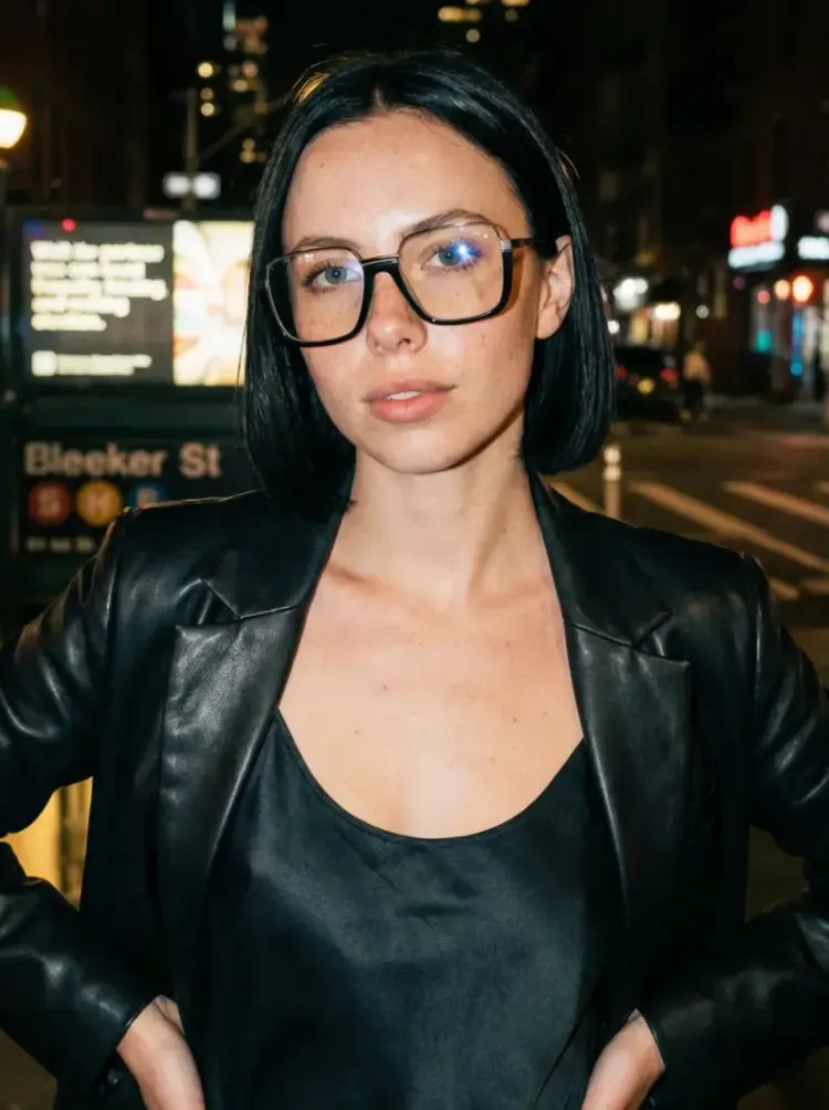 Female model wearing fashion black square acetate eyeglasses on a lit city street at night. SPU: SA0382503