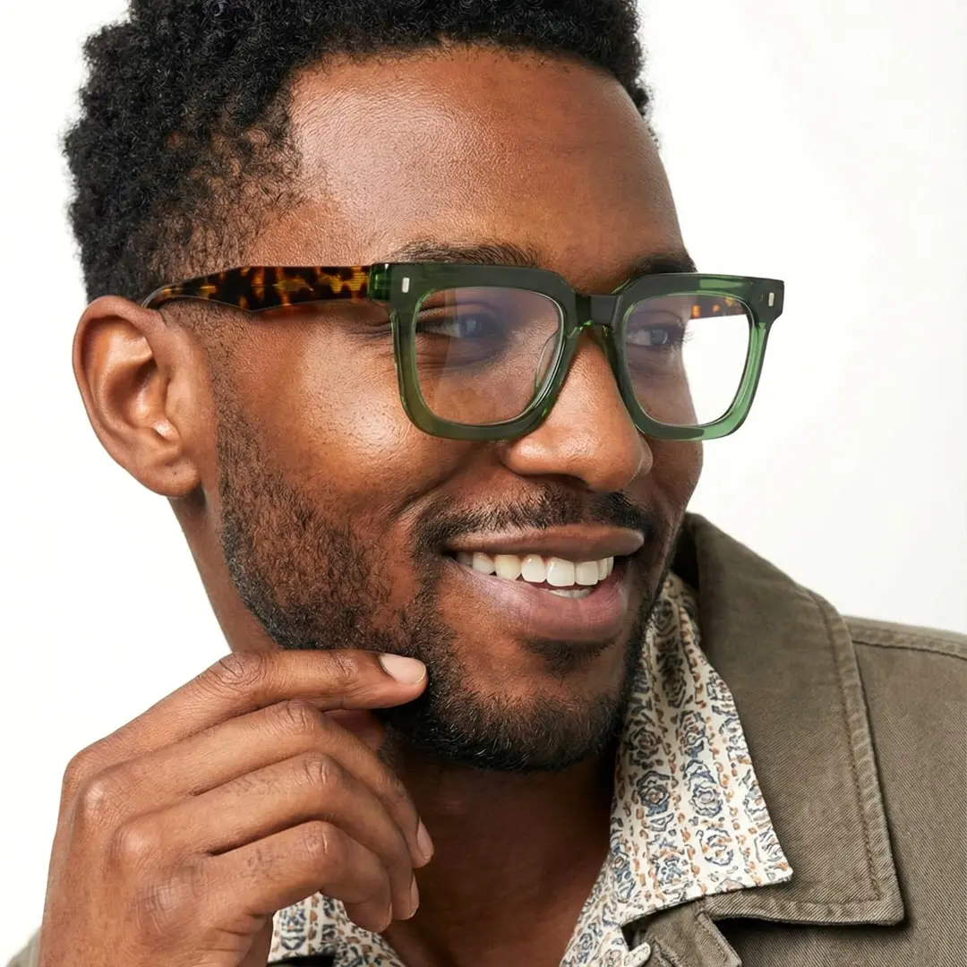 Three-quarter view of male wearing green square eyeglasses, hand near face, smiling, SA0412504