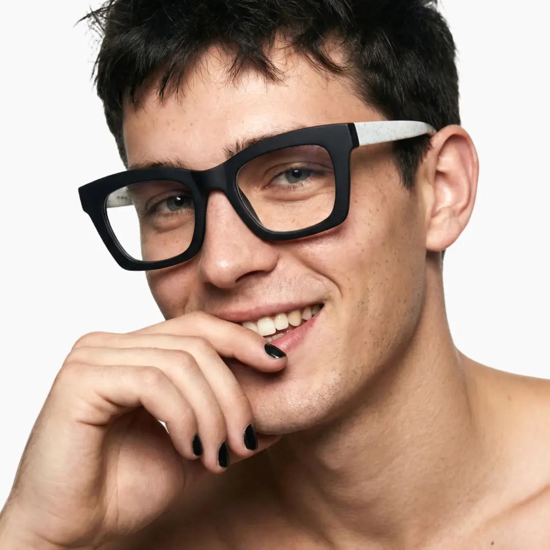 Slightly angled view of male wearing white square eyeglasses, resting chin on hand, smiling, SP0082408