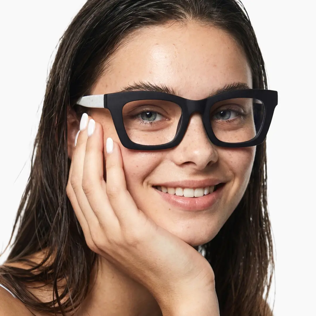 Three-quarter view of female wearing white square eyeglasses, resting chin on hand, smiling, SP0082408