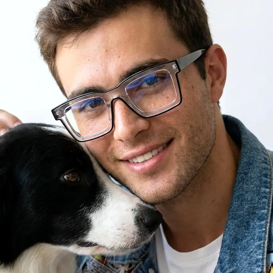 Three-quarter view of male wearing clear square eyeglasses, petting dog, smiling, SR0032307