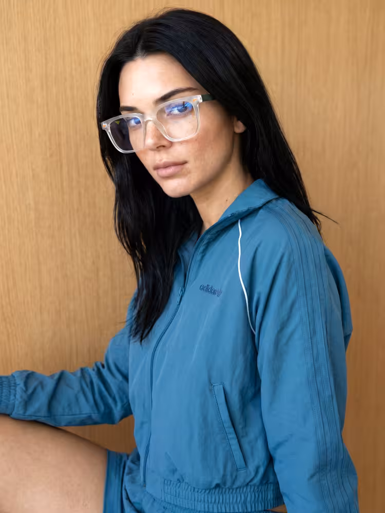 Female model wearing everyday black square TR90 eyeglasses with blue tracksuit against wooden panel background. SPU:SR0122605