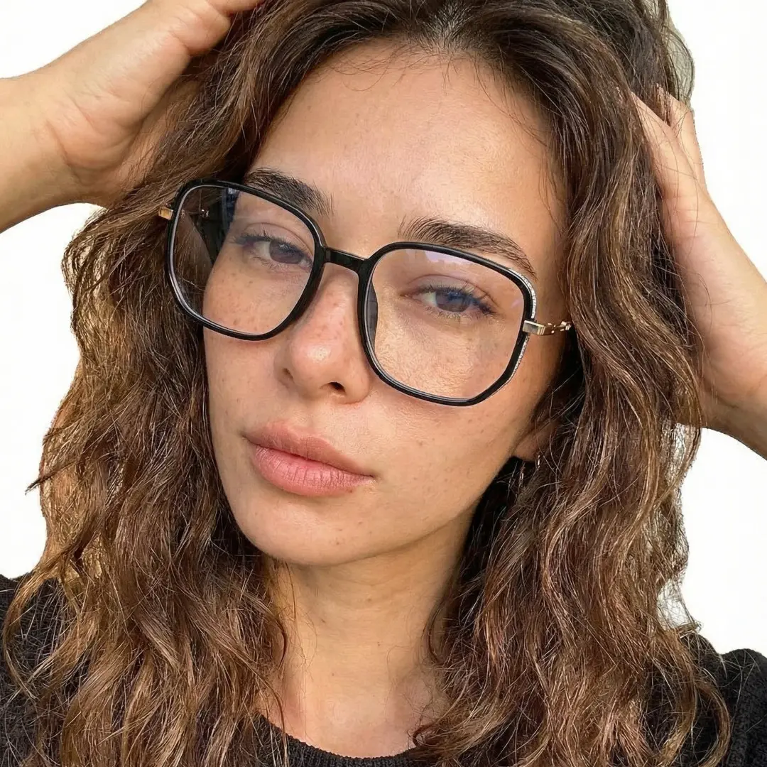 Front view of female wearing vintage black square eyeglasses, hand in hair, natural expression, SR0162409