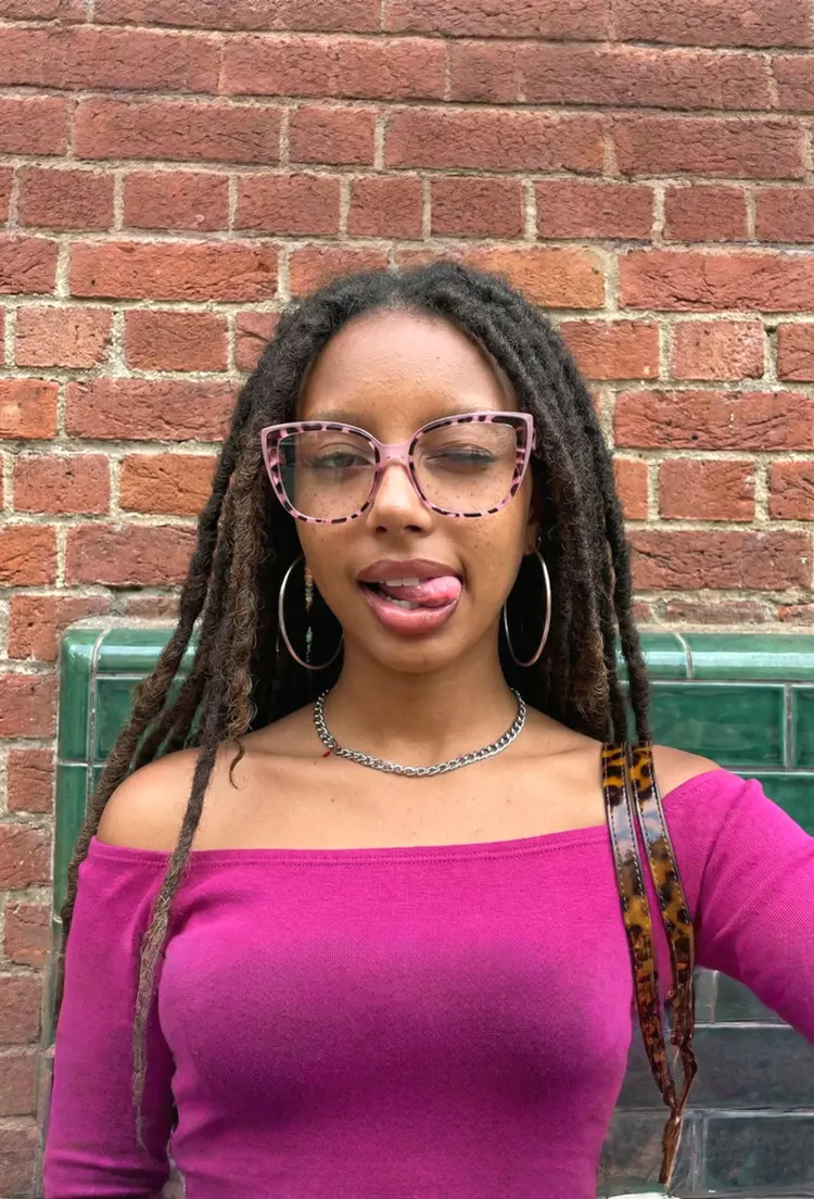 Female model wearing vintage tortoise square tr90 eyeglasses outdoor playfully against a red brick. SPU: SR0202411