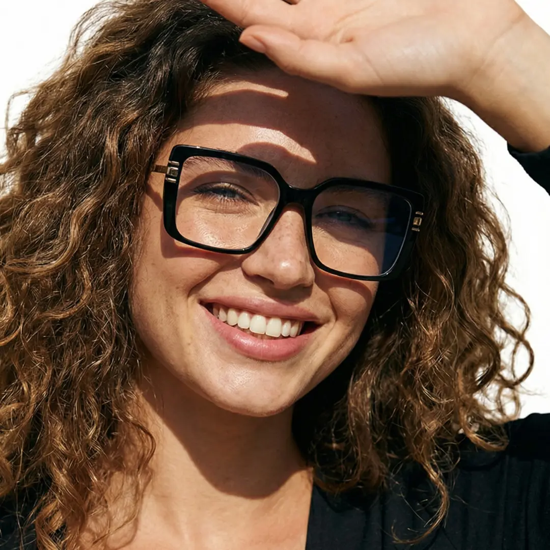 Slightly angled view of female wearing black square eyeglasses, hand in hair, smiling, SR0292508