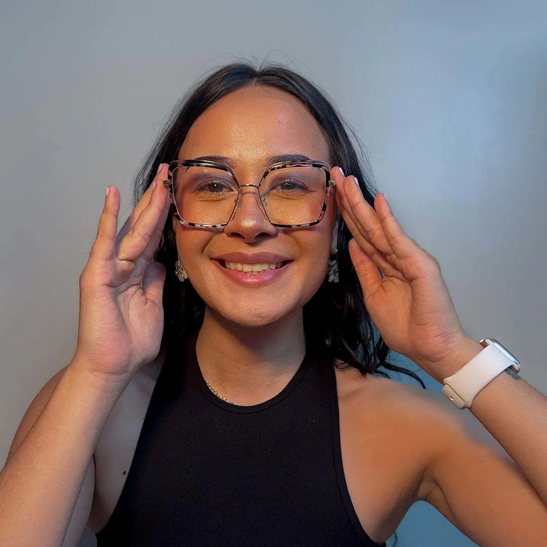 Front view of female wearing tortoise square eyeglasses, holding glasses, soft smile, SR0332503