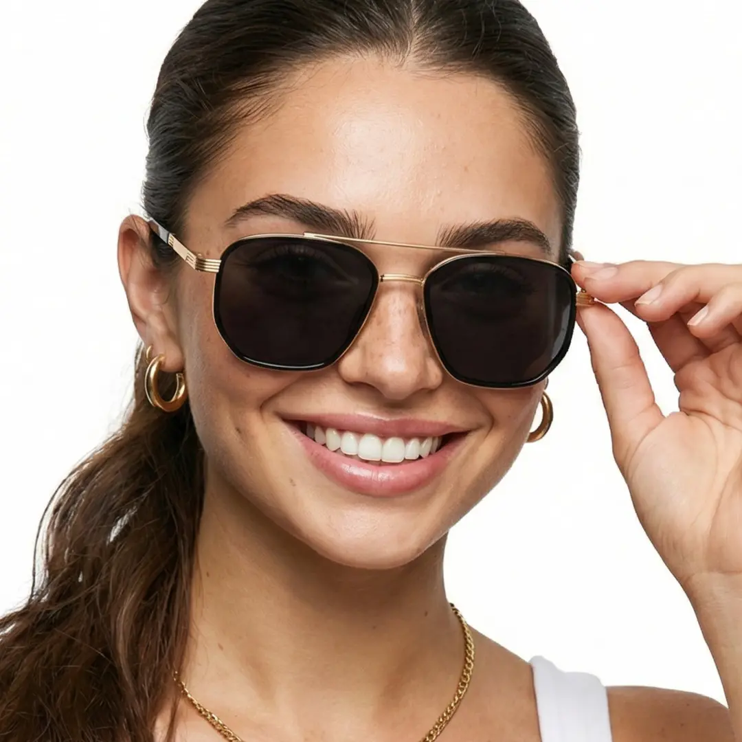 Front view of female wearing gold aviator sunglasses, holding glasses, smiling, AM0622505