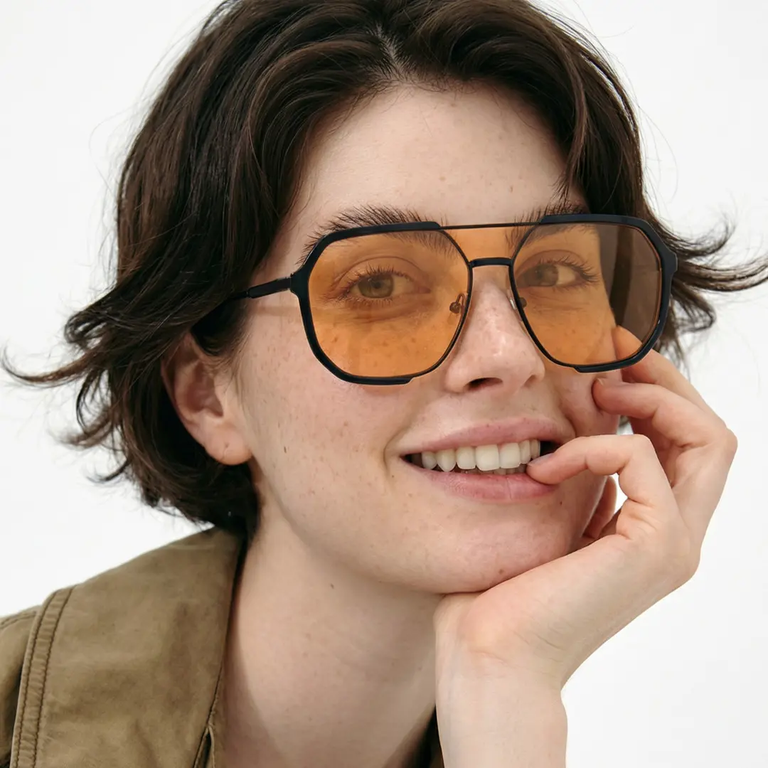 Three-quarter view of fashion female wearing orange aviator sunglasses, resting chin on hand, smiling, AR0042410