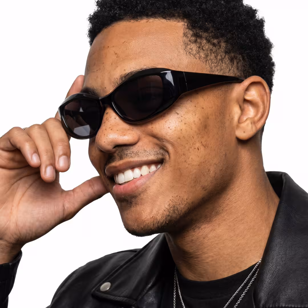 Profile view of male wearing y2k black cat eye sunglasses, touching frame, natural smile, CP0172603