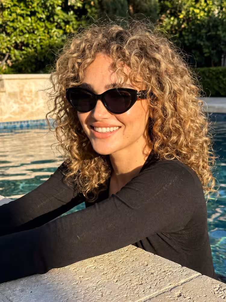 Female model wearing everyday black cat eye tr90 sunglasses by a sunlit swimming pool. SPU: CR0042604