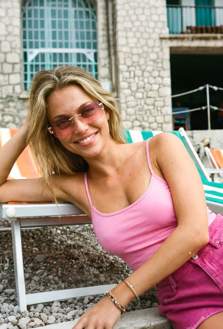 Female model wearing fashion pink rectangle metal sunglasses in a sunny beachside resort. SPU: EM0122410