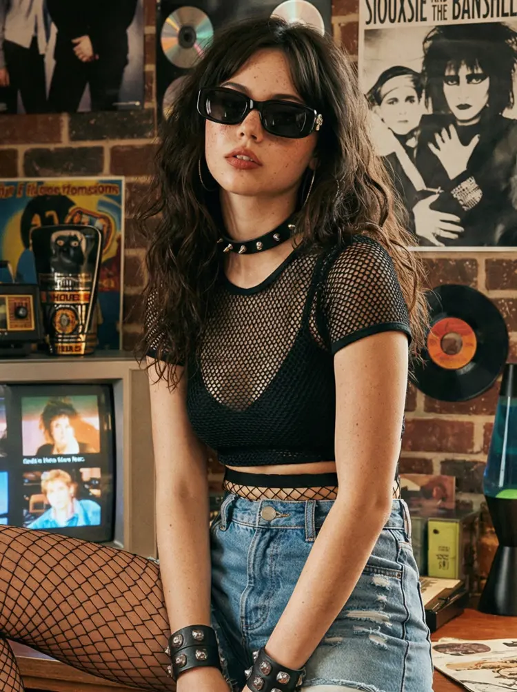 Female model wearing everyday black rectangle pc sunglasses in a retro punk room with a brick wall adorned with vinyl records and music posters. SPU: EP0092511