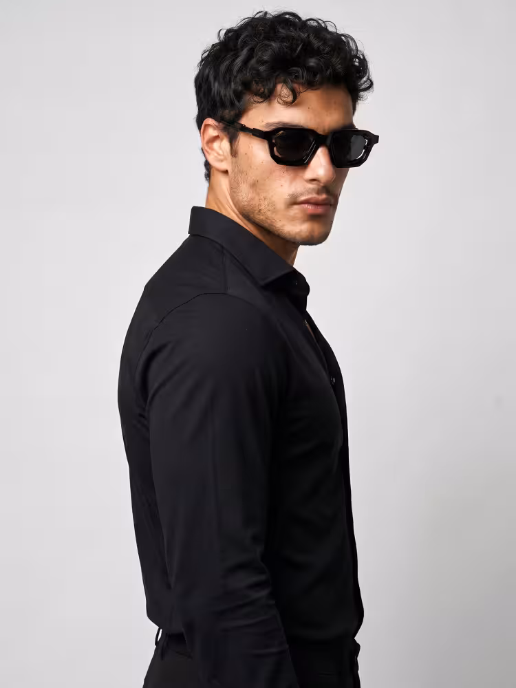 Male model wearing fashion black geometric pc sunglasses in a black dress shirt looking over his shoulder against a plain grey studio background. SPU: GP0482605