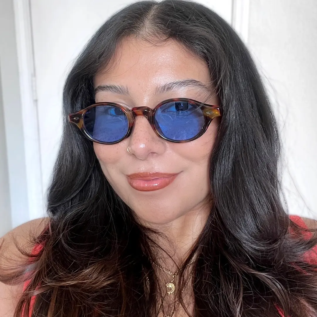 Front view of female wearing tortoise oval sunglasses, smiling, OP0062505