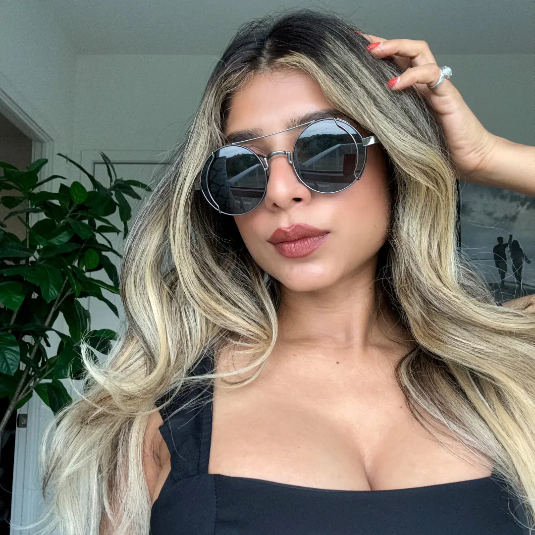 Looking straight ahead view of female wearing steampunk black round sunglasses, hand in hair, soft smile, RM0102303