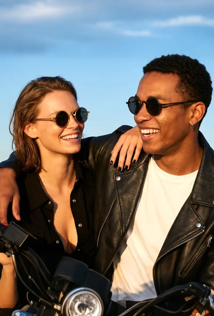 Couple model wearing vintage black and gold round metal sunglasses on a motorcycle outdoors. SPU: RM0162506