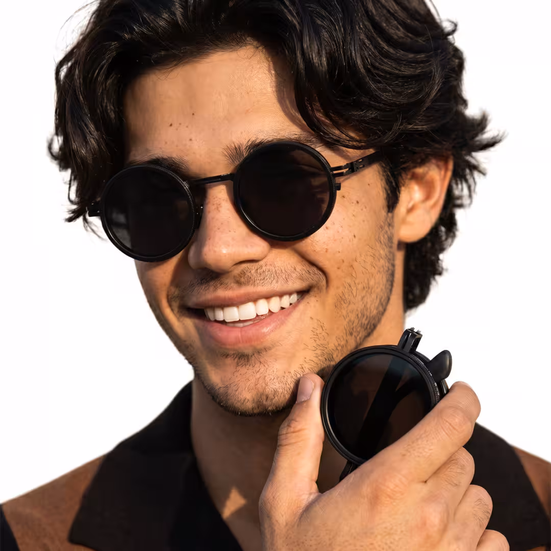 Front view of male wearing steampunk black round sunglasses, holding glasses, smiling, RM0292604