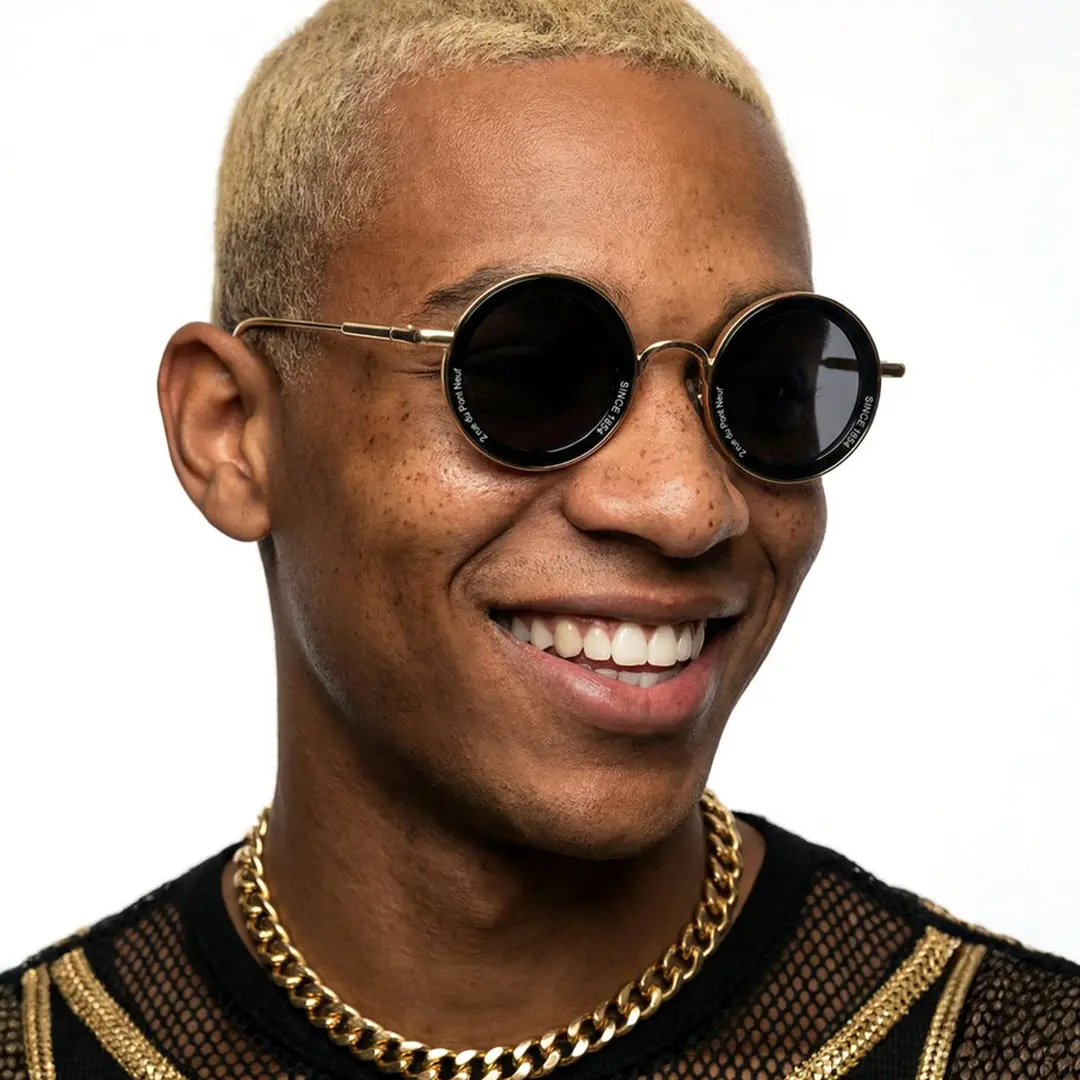 Three-quarter view of male wearing vintage gold round sunglasses, smiling, RM0362504