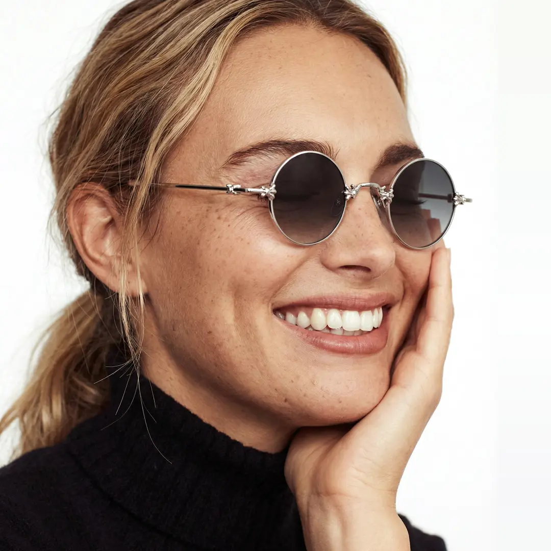 Profile view of female wearing silver round sunglasses, resting chin on hand, smiling, RM0362505