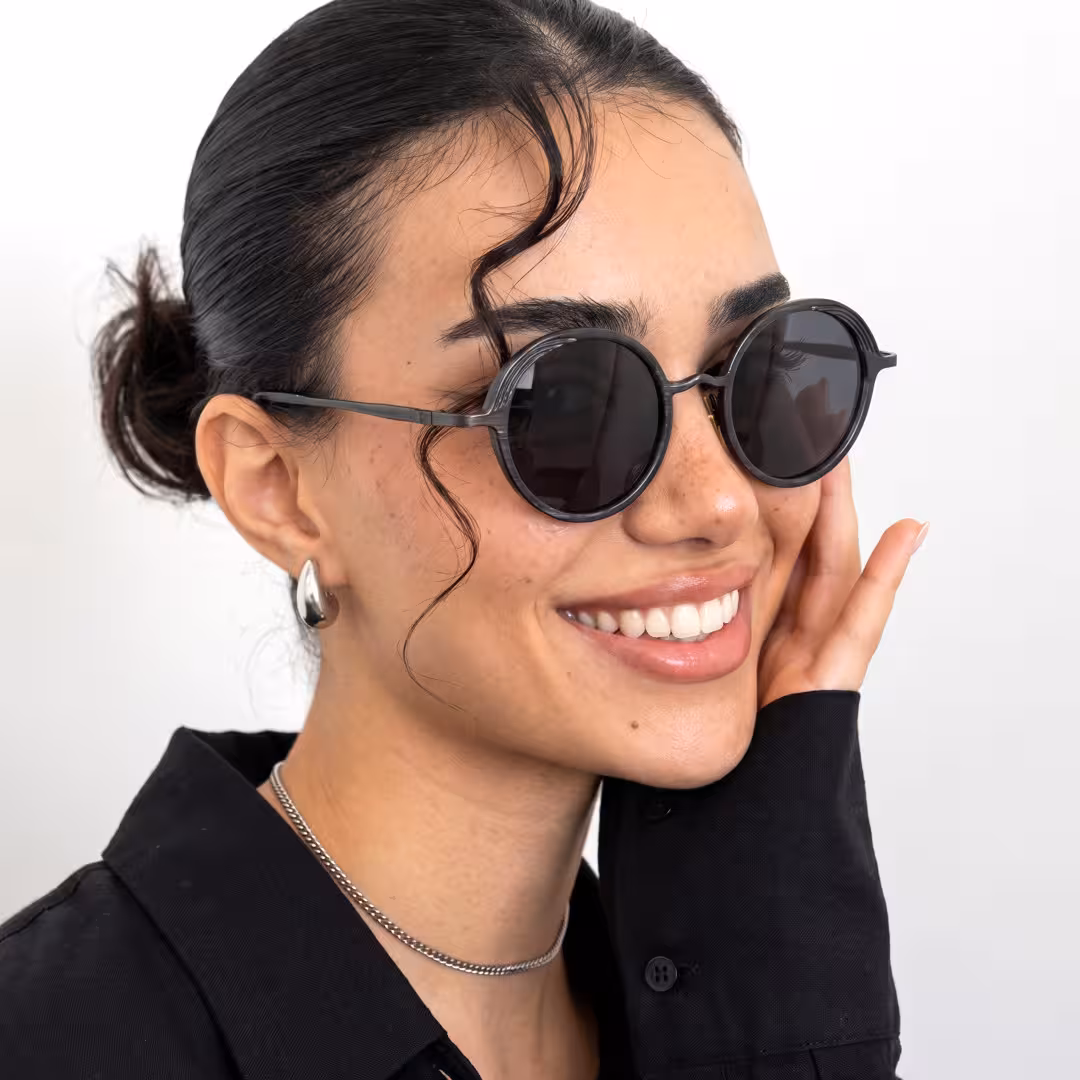 Profile view of female wearing john lennon black round sunglasses, hand near face, smiling, RM0402601