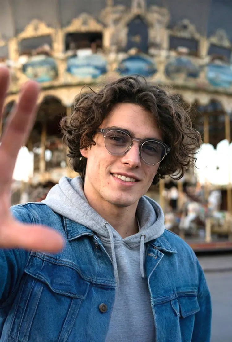 Male model wearing casual grey round tr90 sunglasses in front of a carousel. SPU: RR0062402