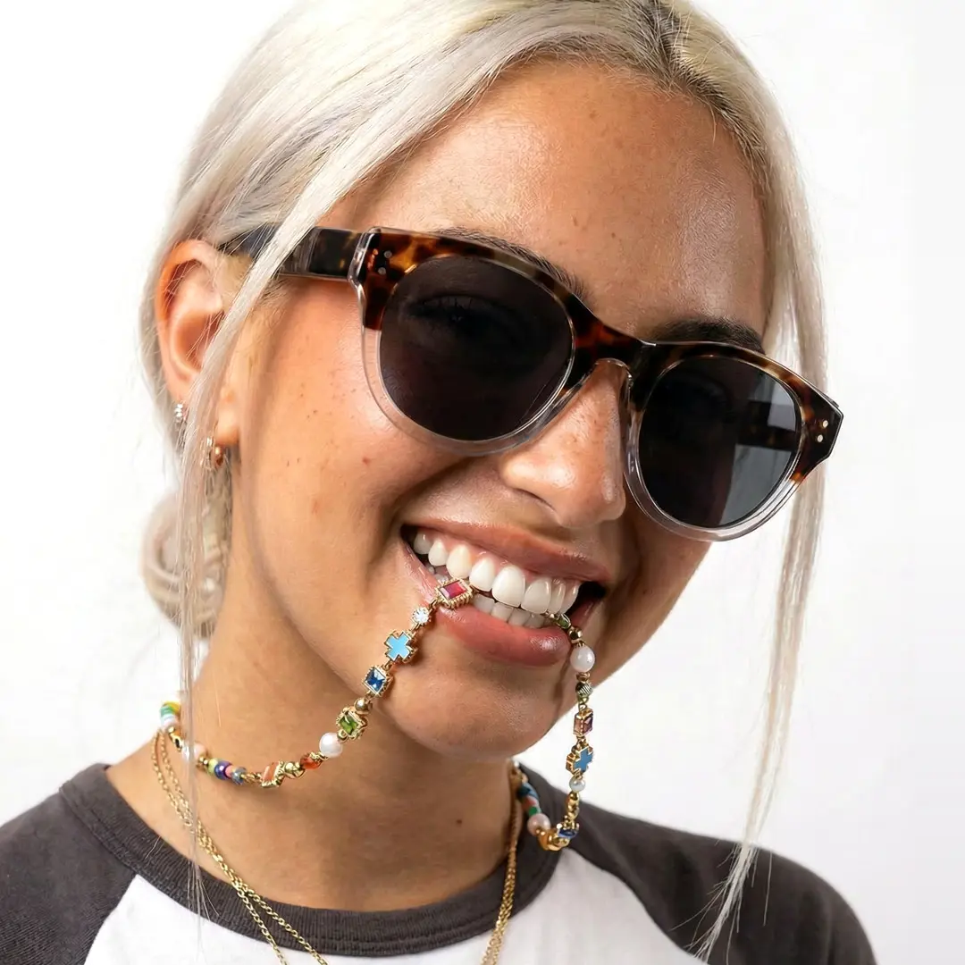 Three-quarter view of female wearing tortoise round sunglasses, mouth biting necklace, smiling, RR0242302