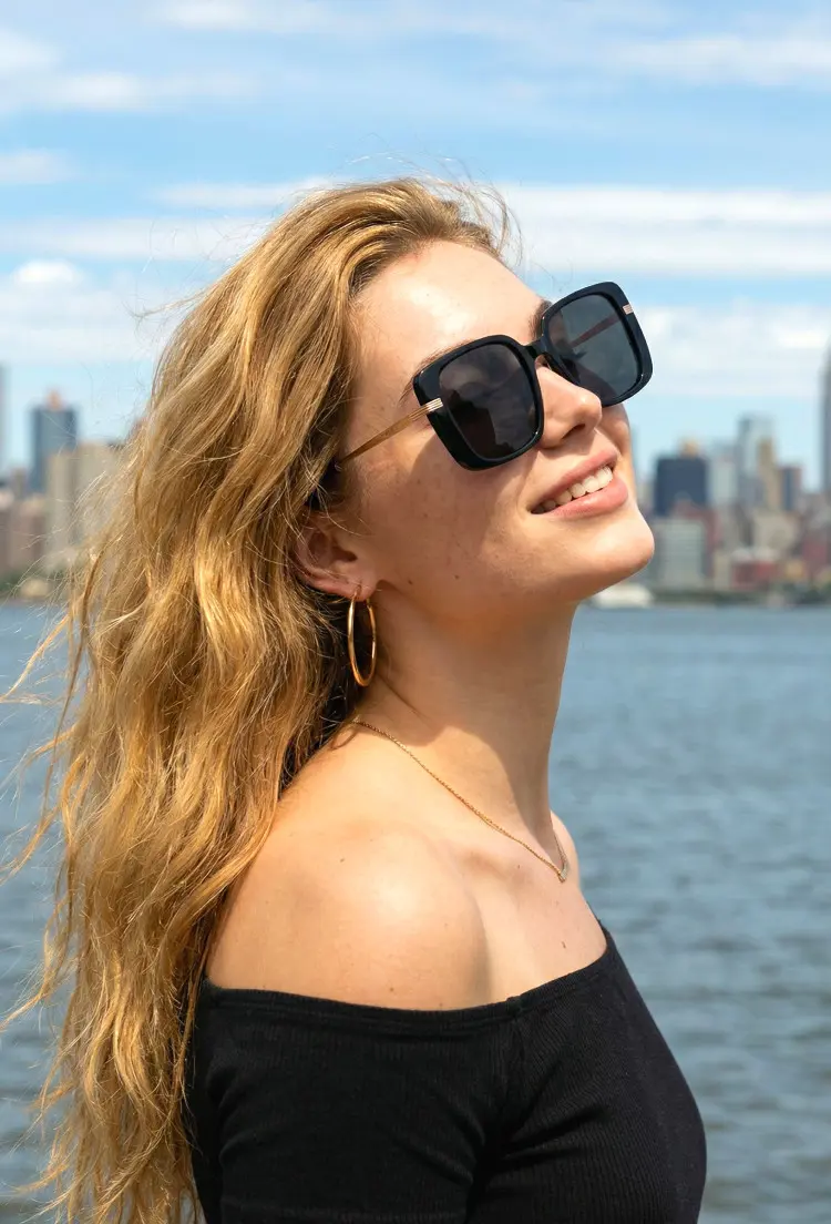 Female model wearing everyday black square acetate sunglasses by a city riverfront with skyline views. SPU: SA0392503S