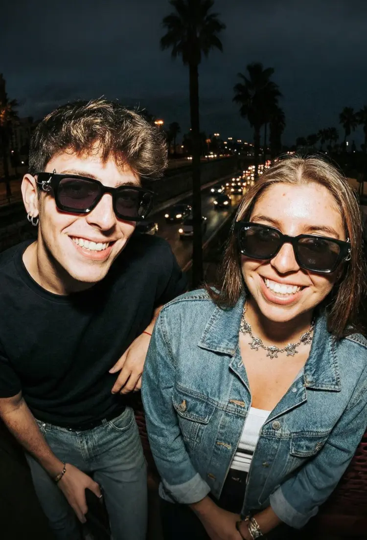 Couple model wearing handcrafted black square pc handcrafted polarized sunglasses in a night city setting. SPU: SP0012603