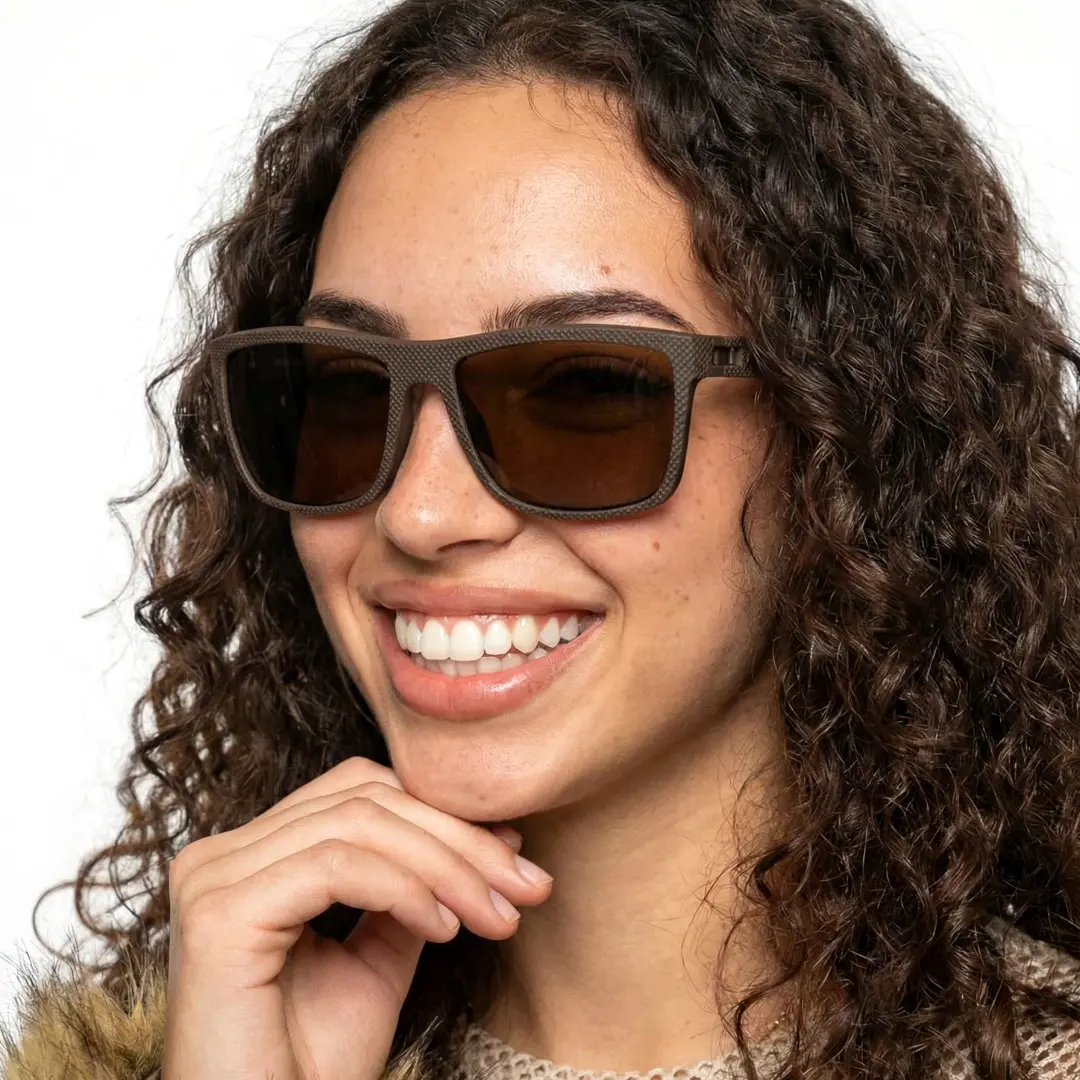 Face close-up view of female wearing brown square sunglasses, resting chin on hand, smiling, SR0072410