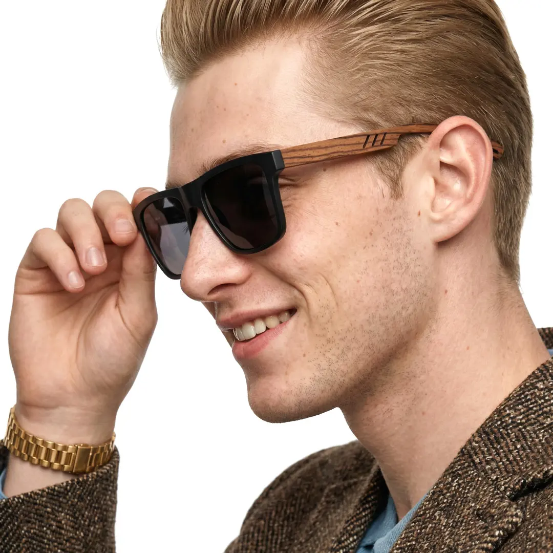 Three-quarter view of male wearing black square sunglasses, holding glasses, smiling, SX0012304